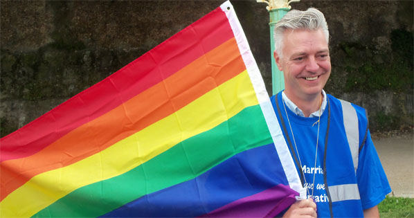 Simon Kirby MP holds gay coloured flag at summer rally on Brighton's seafront